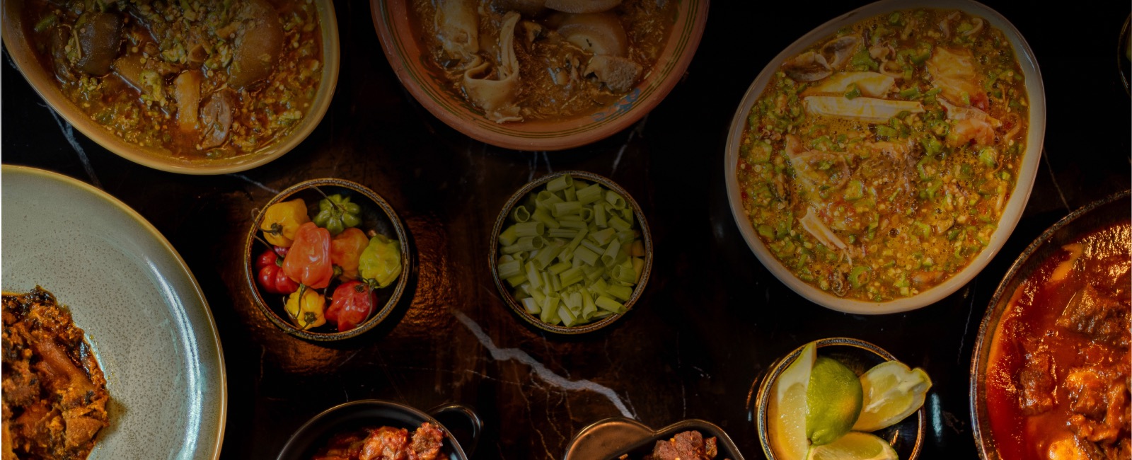 Stews, rice and small dishes set out across a dark table, seen from above