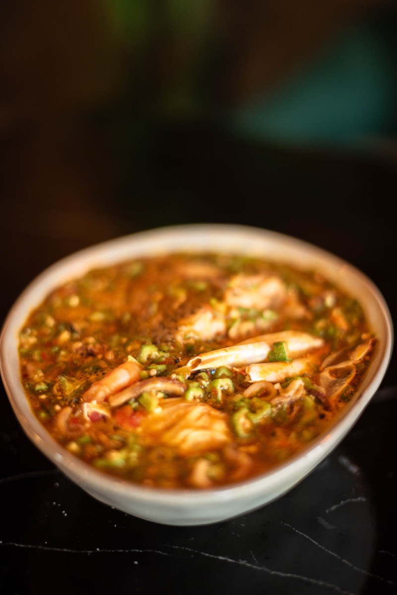 A bowl of red soup with prawns and chopped greens