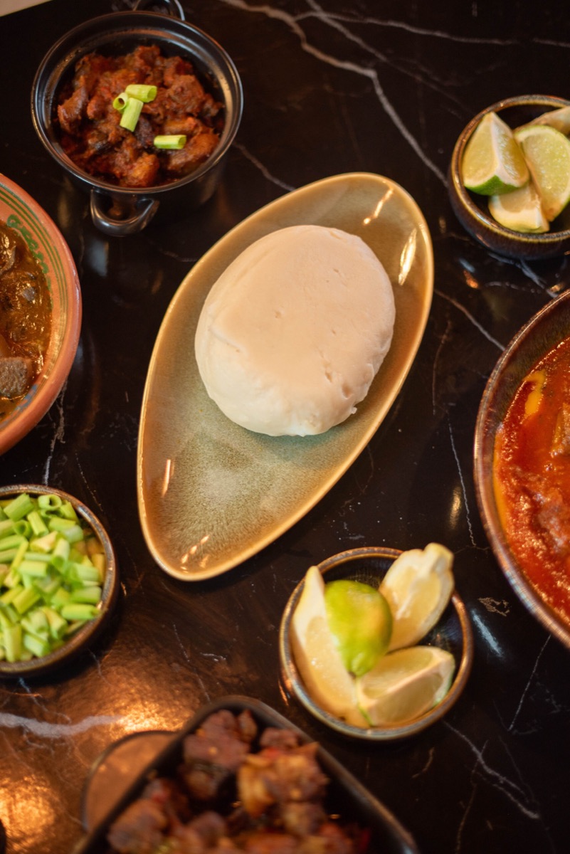 A round of white swallow on an oval dish, surrounded by small bowls of stew, lime and peppered meat