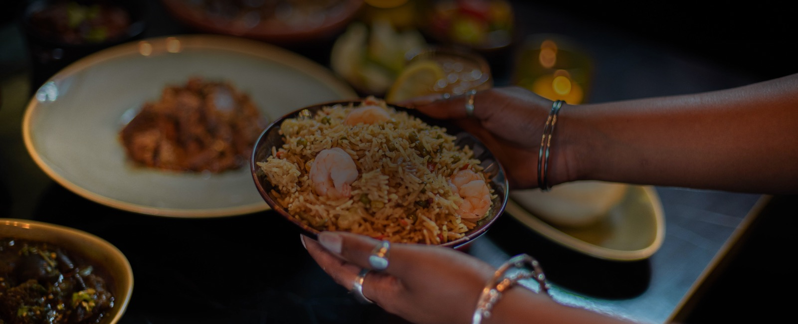 A bowl of fried rice with prawns being passed across a laid table