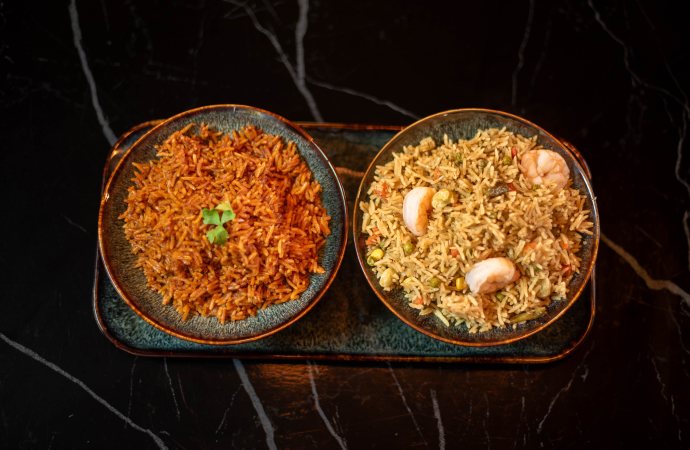 Jollof rice and fried rice with prawns, served in two bowls on one tray