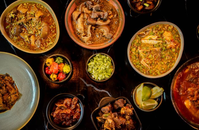 An overhead view of stews, sides, peppers and lime set across a table