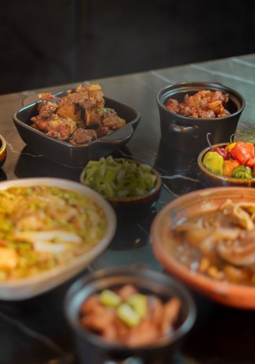 Bowls of stew, greens and peppers set out on a dark table