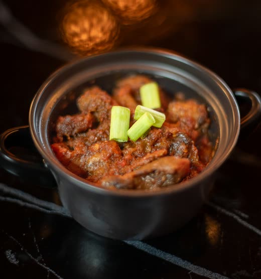 A small cast-iron pot of dark meat stew topped with two batons of leek