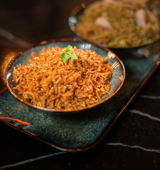 A bowl of red-orange rice with a herb garnish on a dark glazed plate
