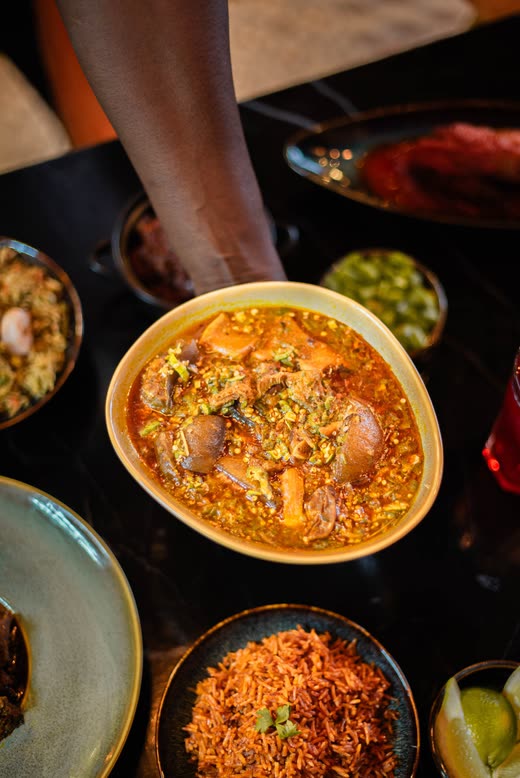 An arm reaching across a laid table towards a yellow bowl of stew