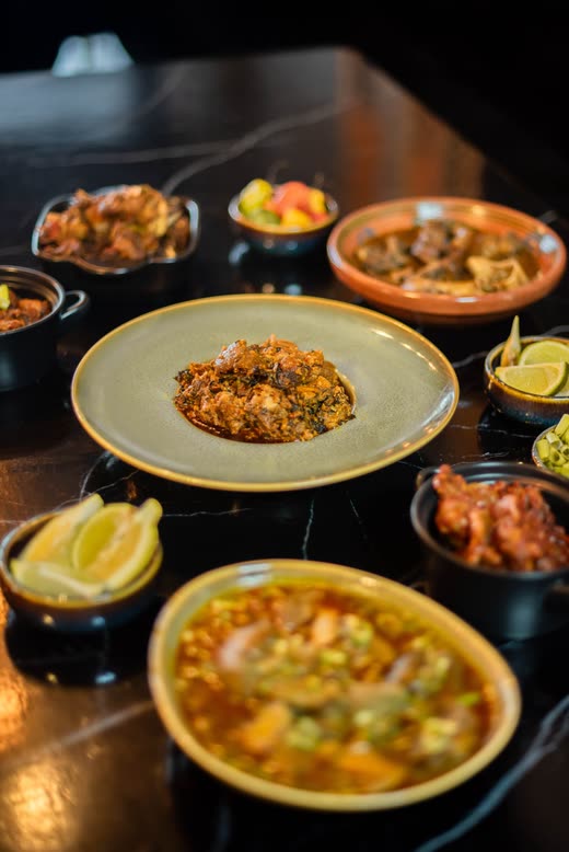 A laid table seen from above — a plate of rice, a bowl of soup, lime wedges and small bowls of relish