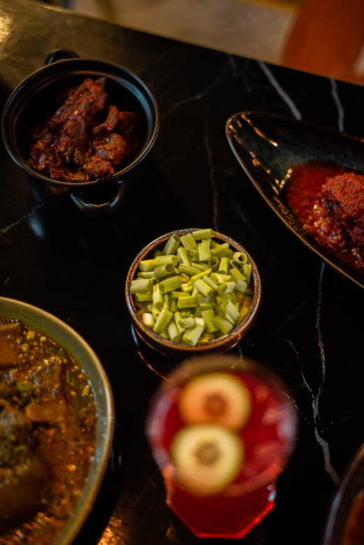 Dark bowls of meat and chopped greens beside a tall red drink