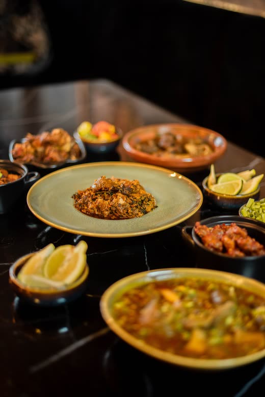 A plate of rice with herbs, surrounded by bowls of stew and lime wedges