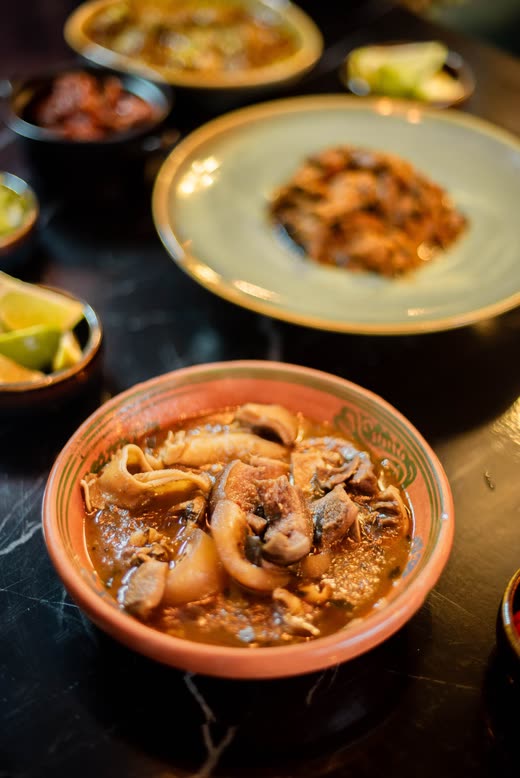 A terracotta bowl of stew on black marble among smaller dishes