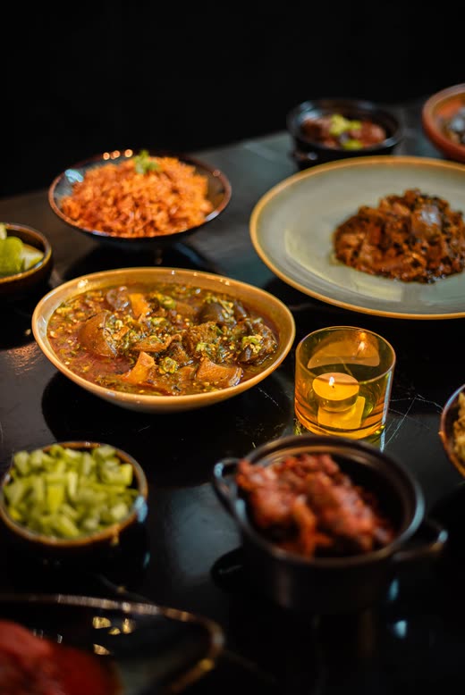 A candle-lit table with bowls of rice, stew and chopped greens