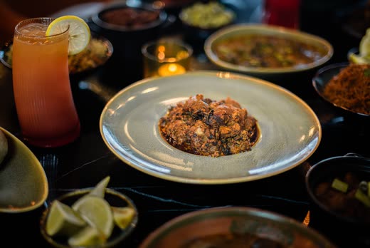 A plate of dark stew on a long table, a tall iced drink beside it