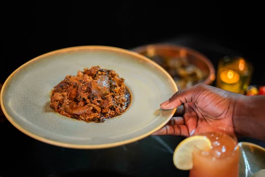 A hand holding out a green-glazed plate of dark stew across the table