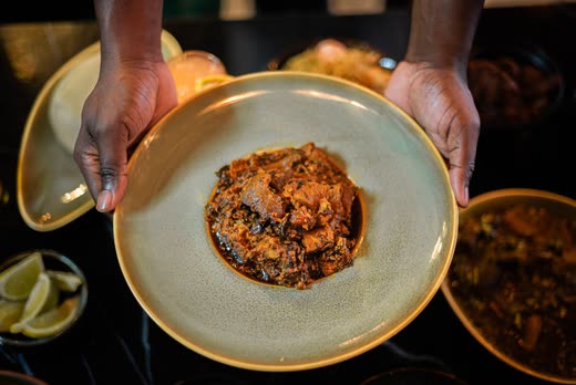 Two hands presenting a plate of dark stew over black marble