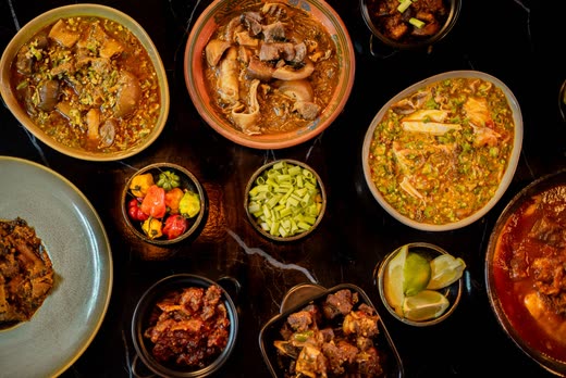 Seen from above — bowls of rice, stew, peppers and greens filling a black marble table