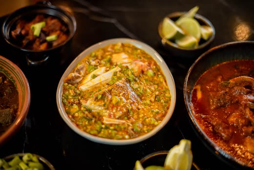 A bowl of stew with prawns and chopped greens, a bowl of red stew beside it