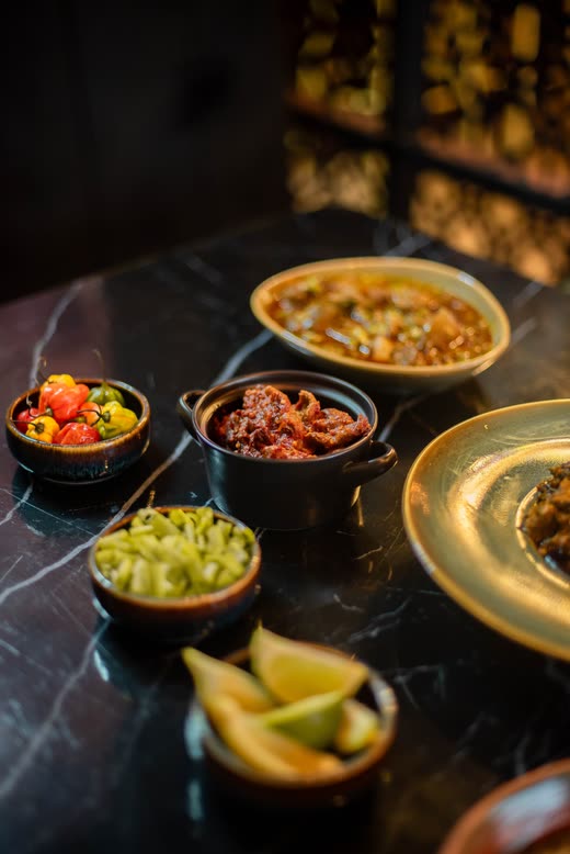 A black marble table with bowls of peppers, meat and greens around a green-glazed plate