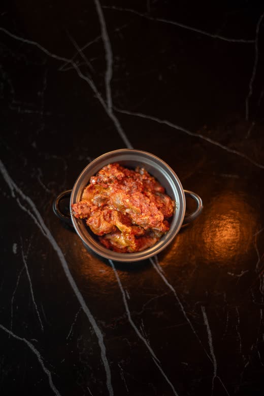 A small metal pot of red pepper relish alone on black marble