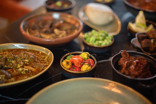 A table of shared bowls — stew, greens, peppers and dark meat