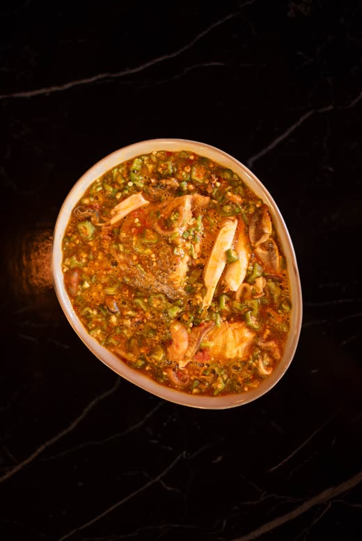 Seen from above — a wide bowl of stew with prawns and chopped greens on black marble