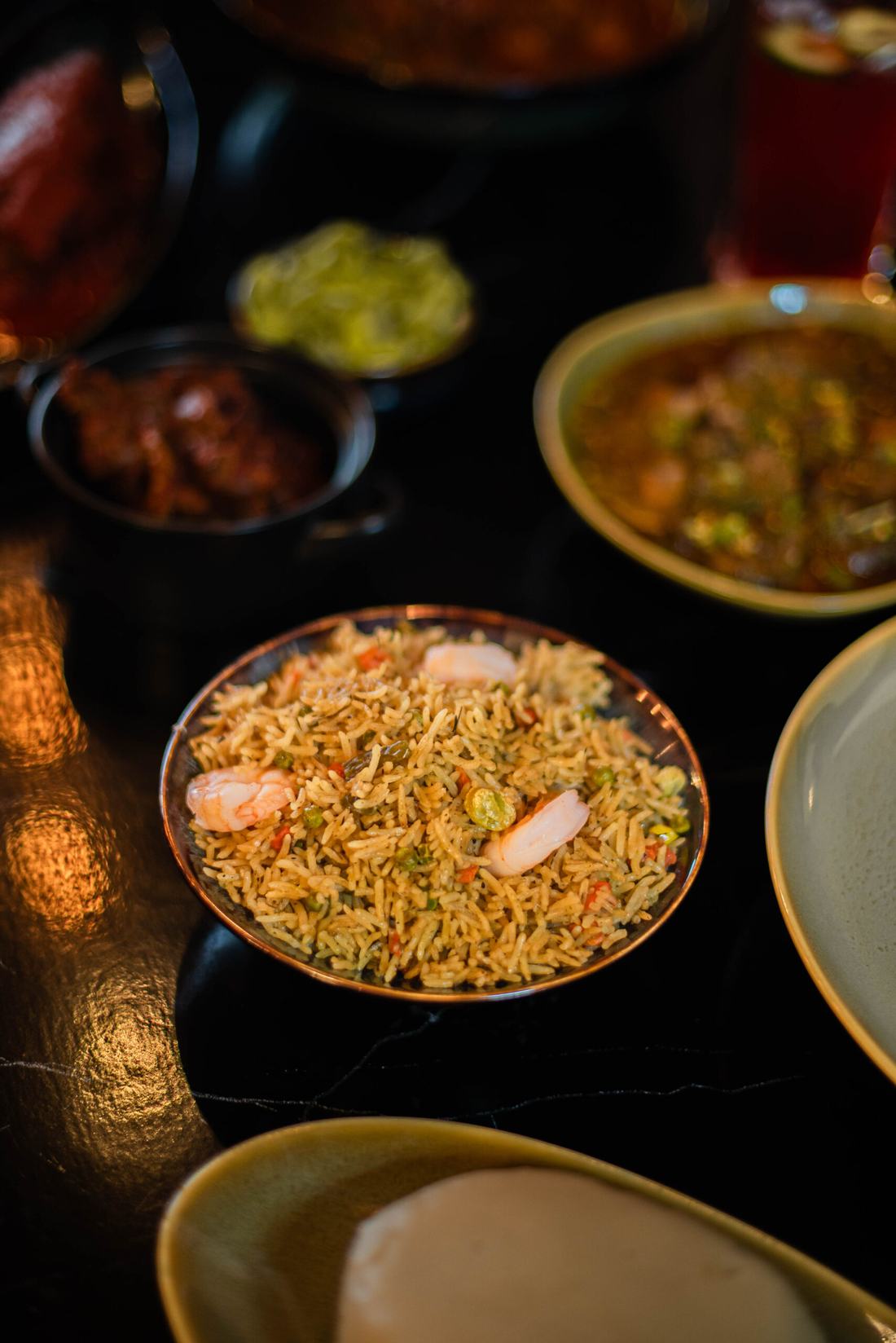 A bowl of fried rice with prawns among other dishes on a table