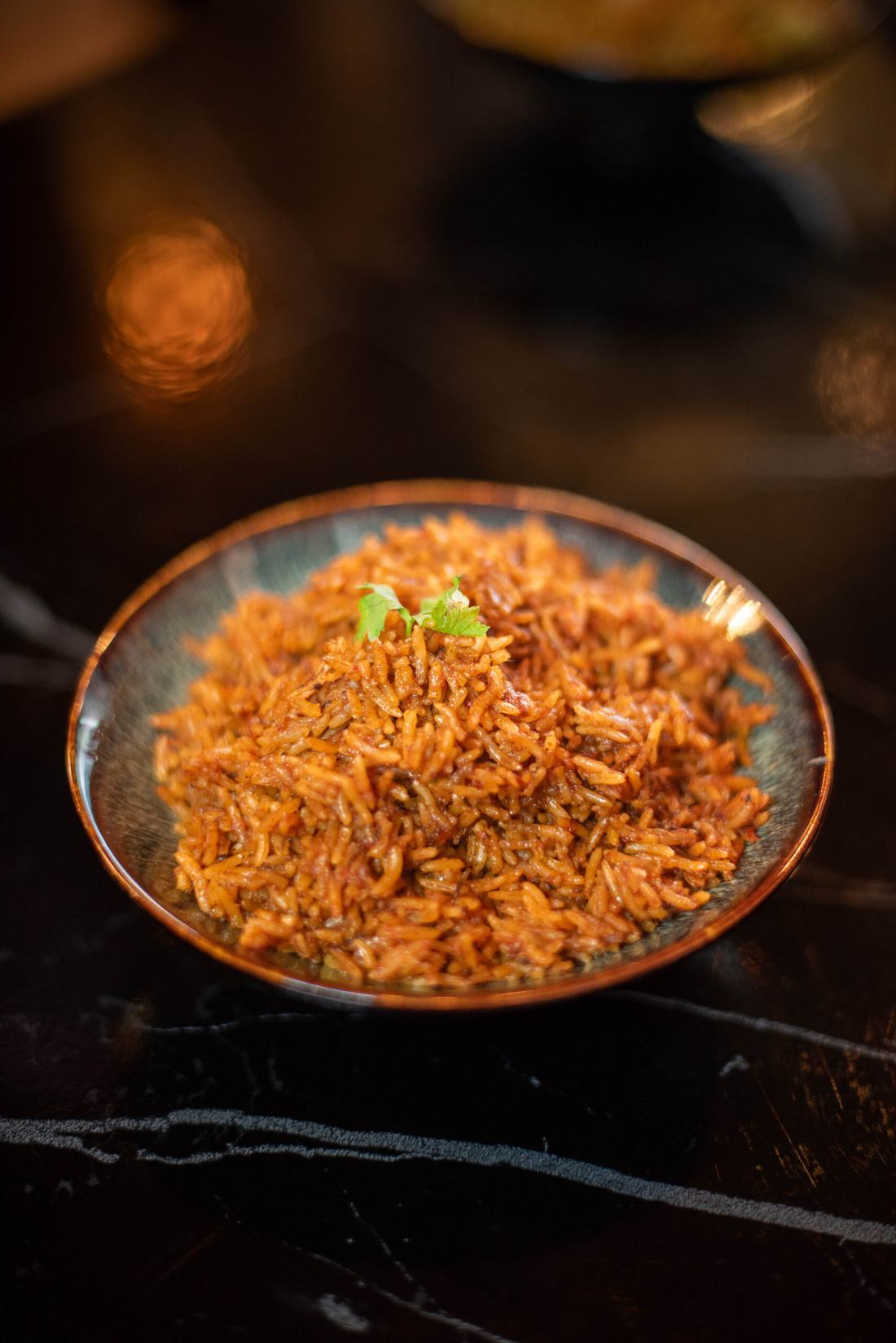 A bowl of jollof rice topped with a sprig of coriander